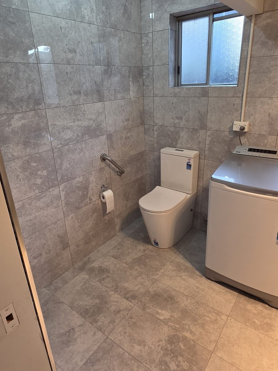 Accessible bathroom with a grab rail beside the toilet, level hobless shower entry and a single continuous tiled floor throughout
