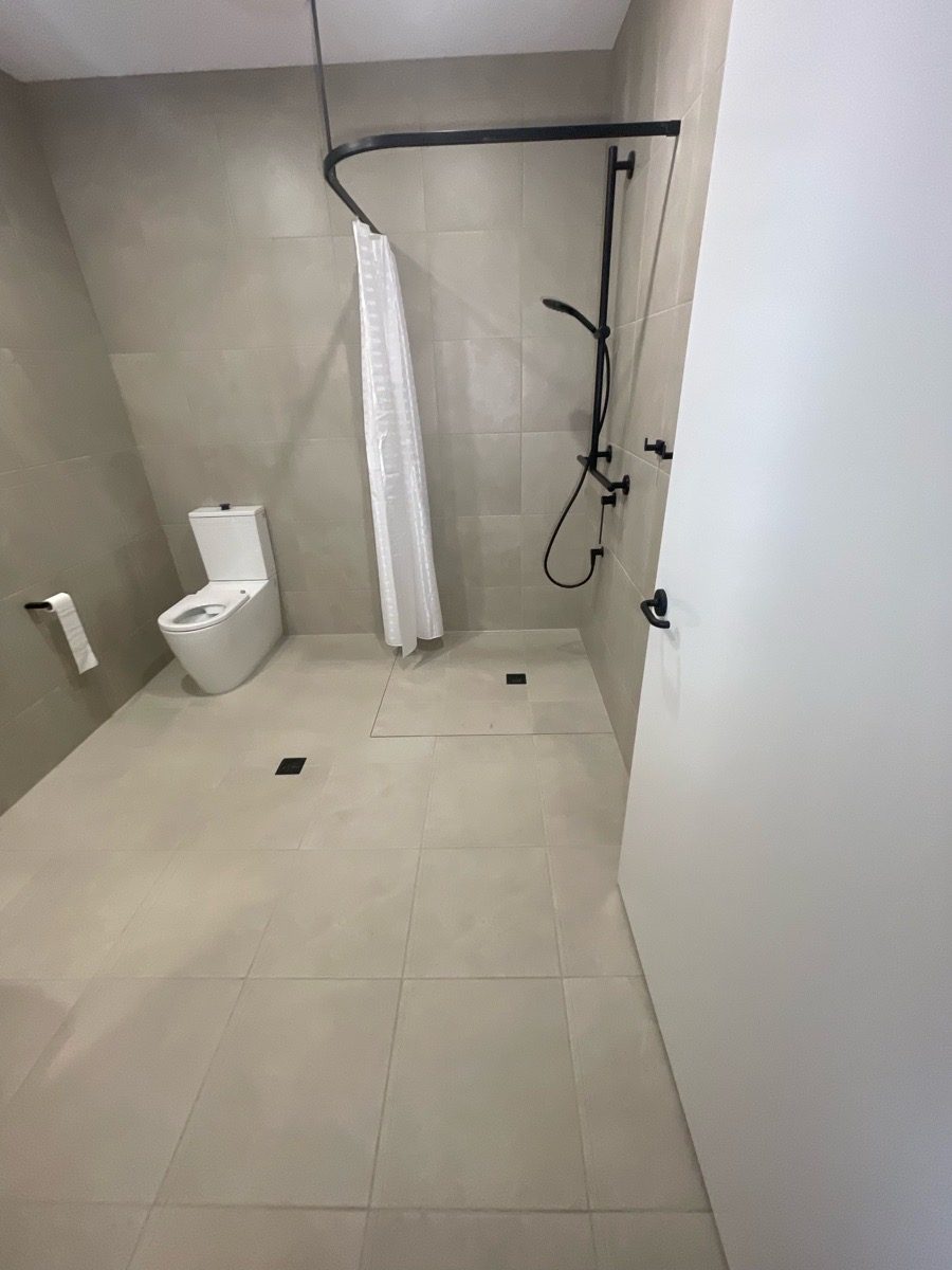Accessible ensuite with hobless shower, curtain rail, handheld shower on a vertical rail and a grab rail beside the toilet