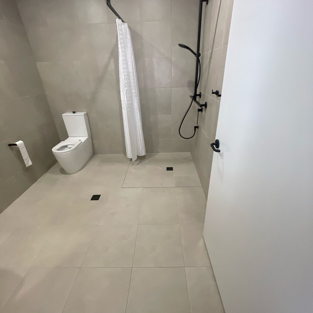 Completed NDIS bathroom modification at Pascoe Vale South: hobless level-access shower with curtain rail, handheld shower and a grab rail beside the toilet