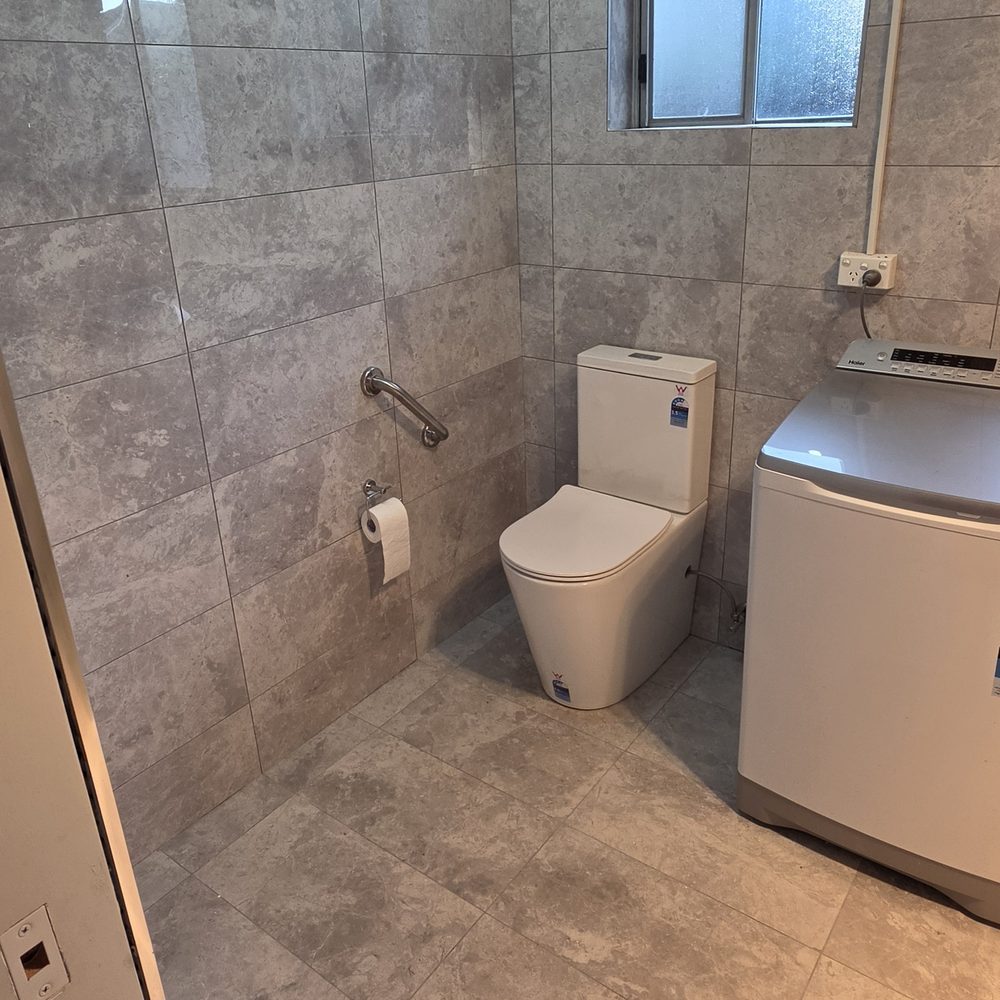 Completed NDIS bathroom modification: grab rail beside the toilet, level hobless shower entry and a single continuous tiled floor